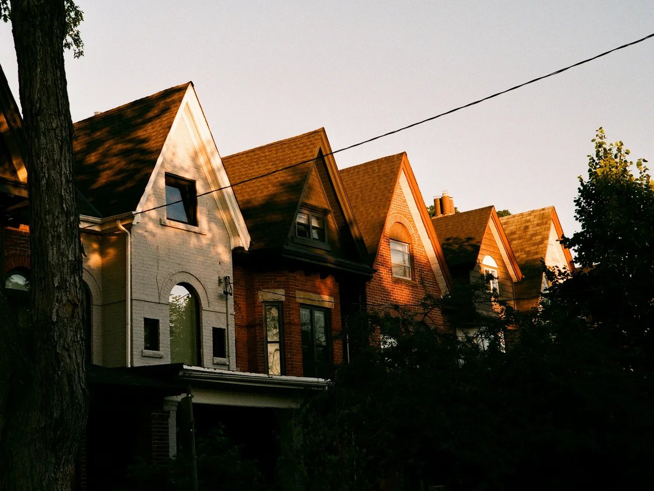 A row of older brick homes with steep gables catching the warm evening light